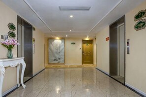 Vestíbulo de hotel con piso de mármol, dos ascensores, una recepción y un elemento decorativo en la pared.