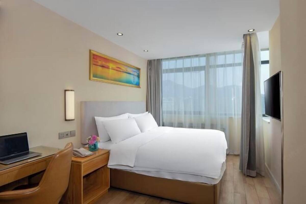 Una habitación de hotel con una cama, un escritorio con una computadora portátil, un televisor y un cuadro en la pared.