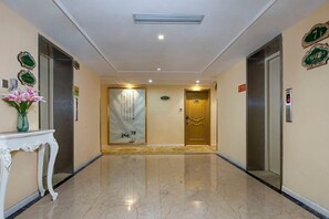 A hotel lobby with a marble floor, two elevators, a reception desk with a vase of flowers, and a wall with a sign. - Vienna 3 Best Hotel (inan Changqing University Town) (Jinan)