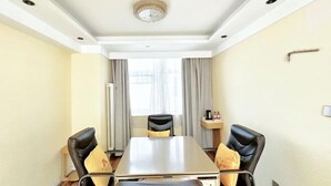 Habitación de hotel con una mesa de comedor, cuatro sillas, una mesita auxiliar y una ventana con cortinas.