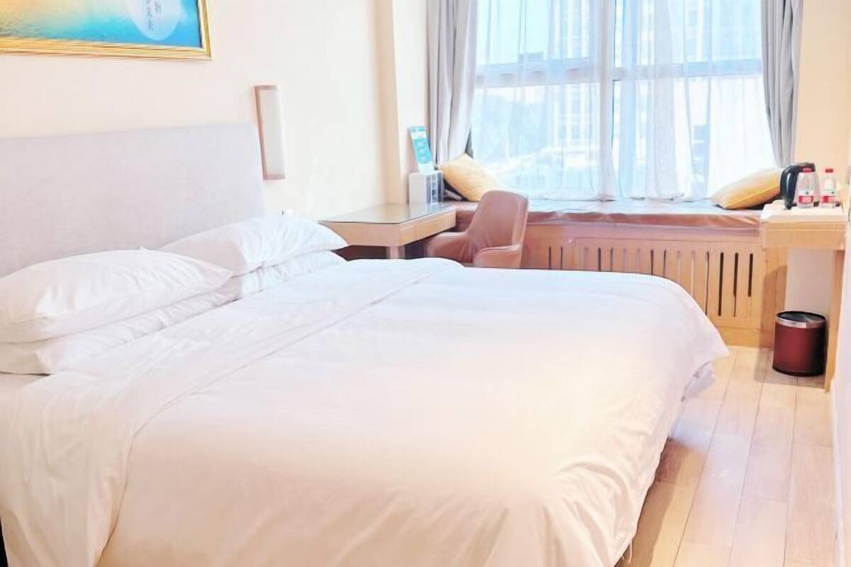 Habitación de hotel con una cama grande, un escritorio con silla, un radiador y una ventana con cortinas.