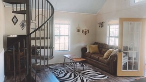 A living room with a spiral staircase, a zebra-patterned rug, a brown leather sofa, and a door with a glass panel. - Fairytale Forest River Cabin (Caledonia)