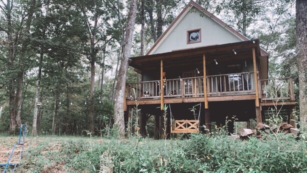 A cabin with a wooden deck and a small porch, surrounded by dense forest. - Fairytale Forest River Cabin (Caledonia)