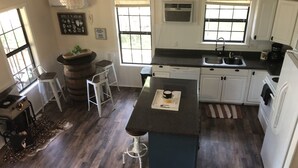 A kitchen with white cabinets, a black countertop, and a wooden floor. There are two bar stools, a coffee maker, and a rug. - Fairytale Forest River Cabin (Caledonia)