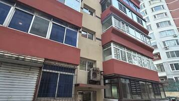 A multi-story residential building with a red and beige facade, large windows, and balconies.