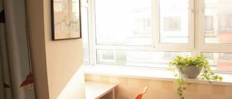 A room with a window, a chair, a potted plant, and a framed picture on the wall.