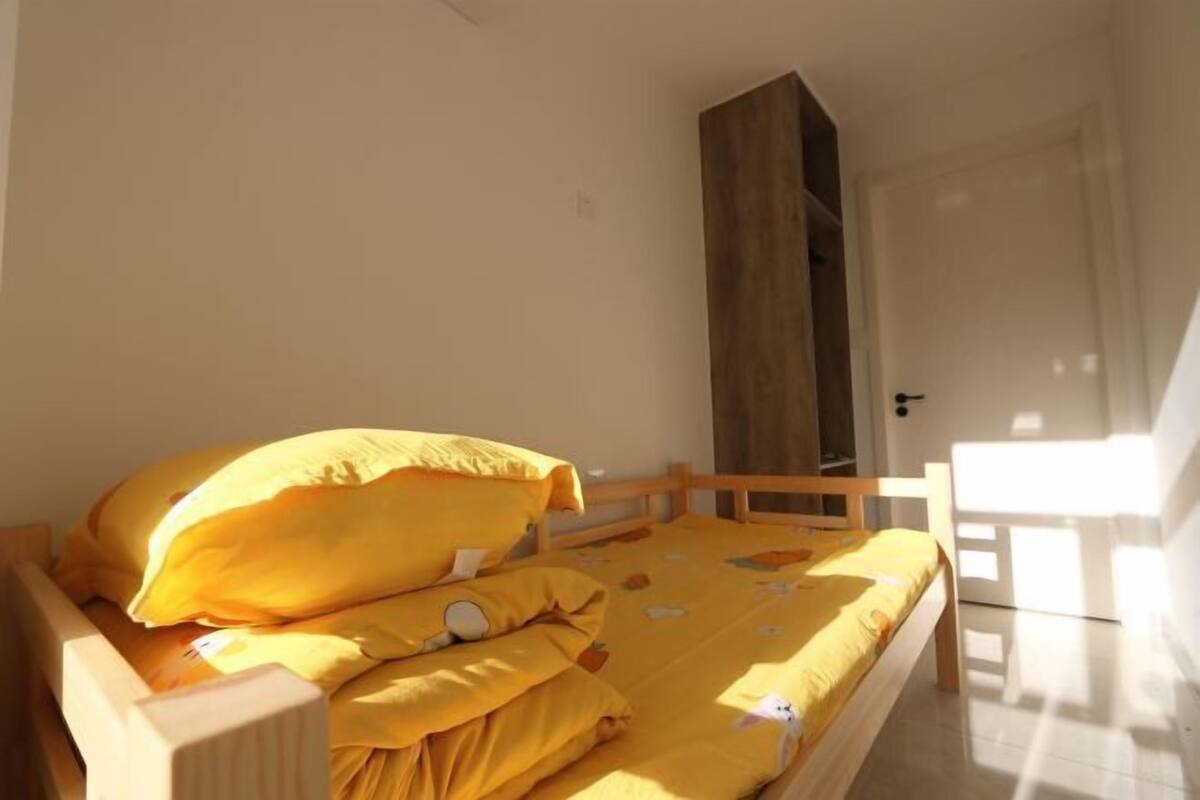 Une chambre à coucher avec un lit en bois, une literie jaune et une porte donnant sur une autre pièce.