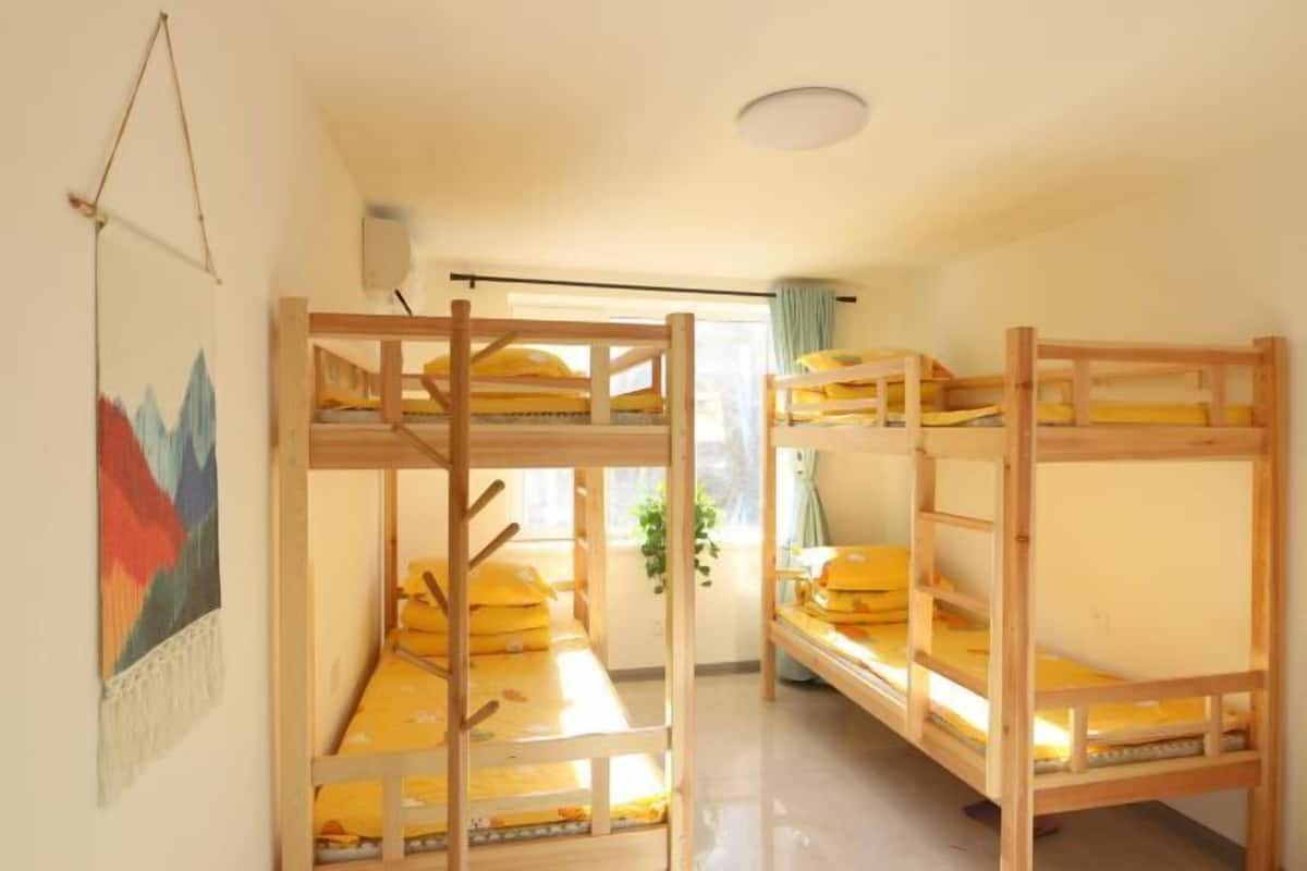 Une pièce avec des lits superposés, une fenêtre avec des rideaux et un luminaire fixé au mur.