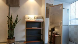 A compact room with a sliding door leading to a kitchen, a potted plant, and a shelving unit with a folded blanket. - Shenyang Chang Kuan Gao Hostel (Shenyang)