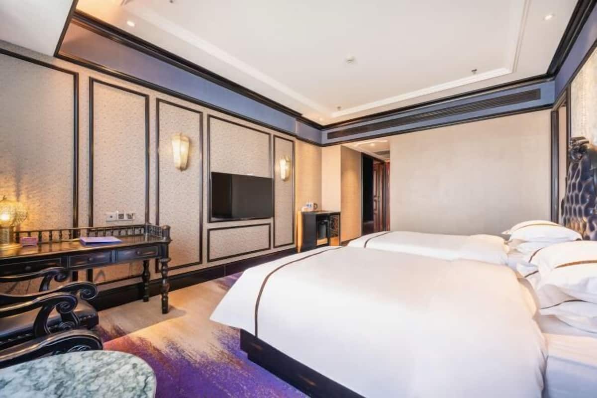 A hotel room with a large bed, a desk with a chair, a flat-screen TV, and a small table.