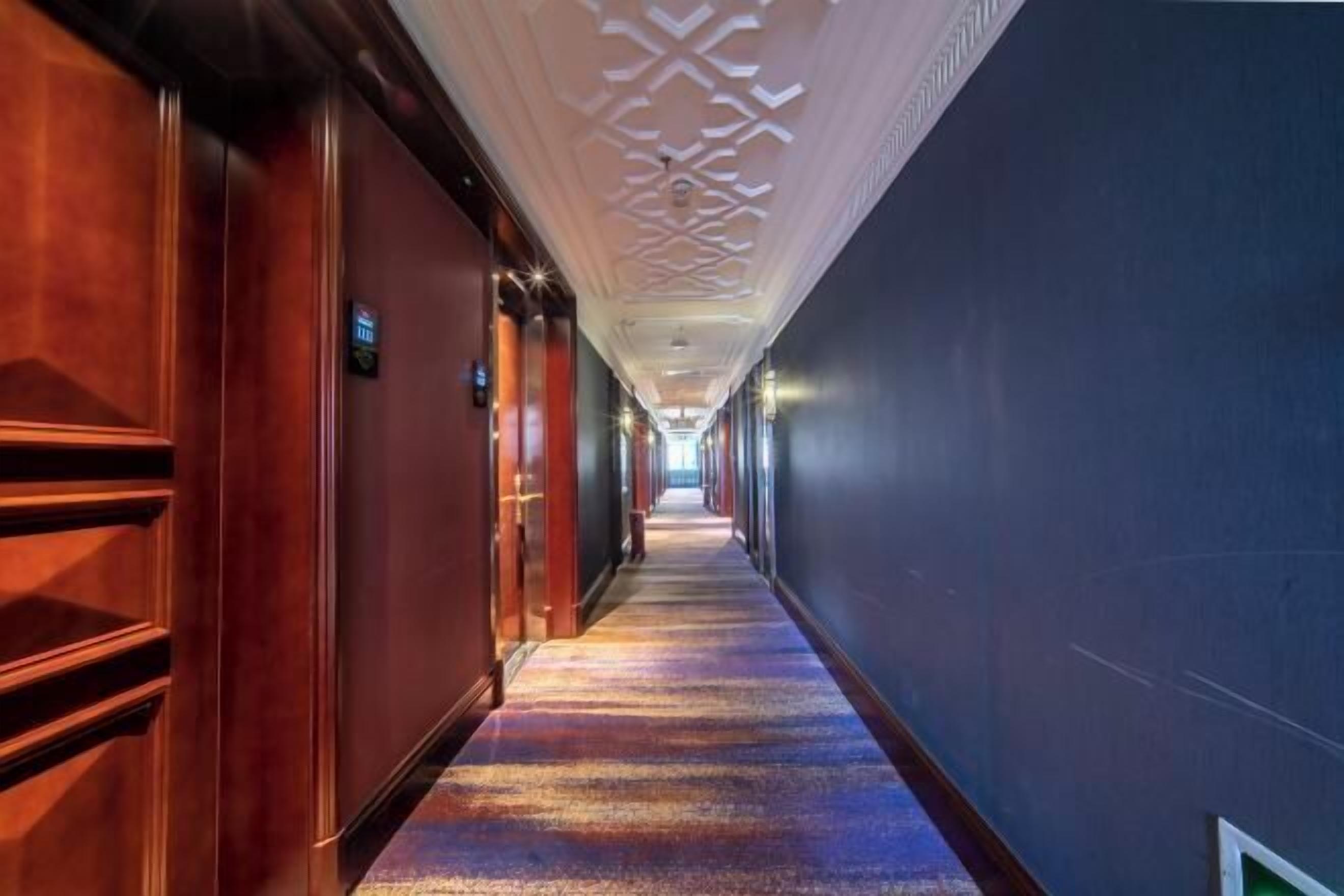 Un pasillo de hotel con puertas de madera, techo estampado y suelo alfombrado.