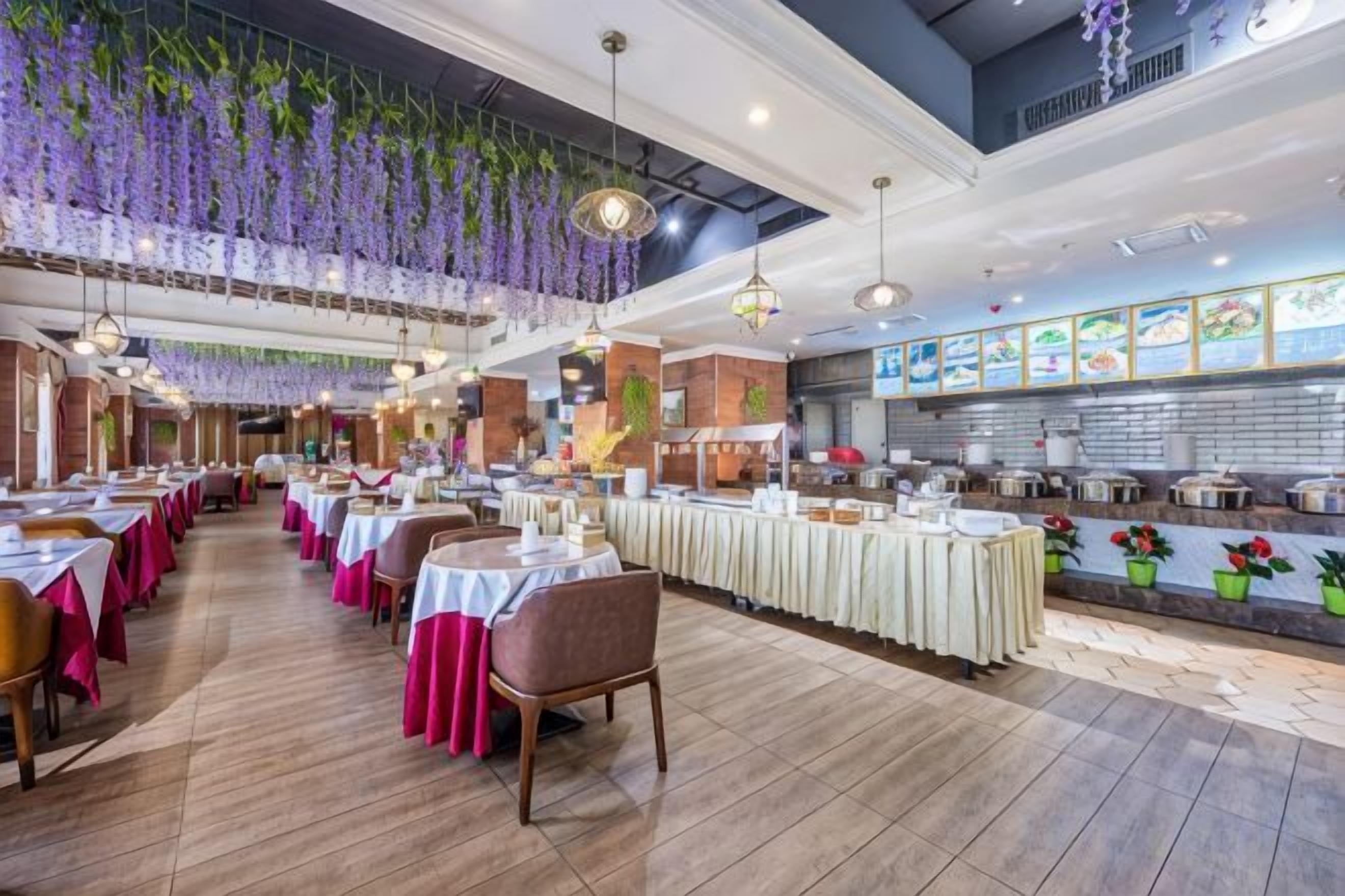 A restaurant with multiple dining tables, hanging plants, and a kitchen area.
