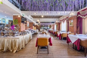 A restaurant with multiple dining tables, hanging purple decorations, and a brick wall.