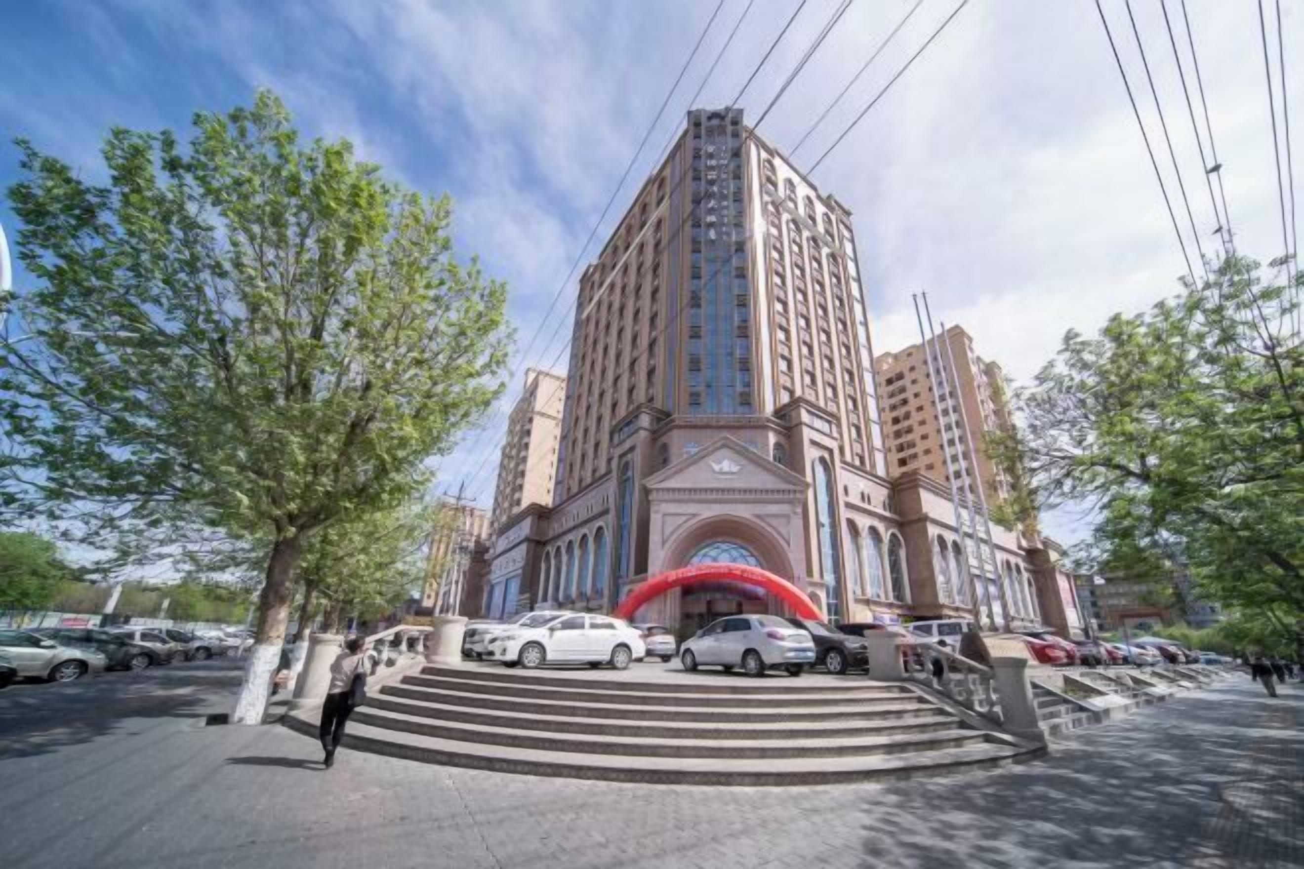A multi-story hotel with a prominent entrance, a red archway, and a parking area with several cars.