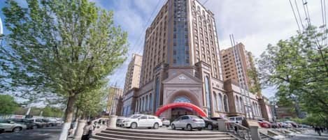 A multi-story hotel with a prominent entrance, a red archway, and a parking area with several cars.