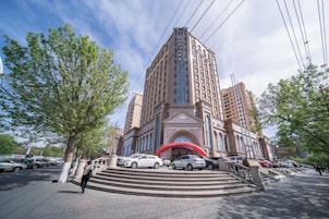 A multi-story hotel with a prominent entrance, a red archway, and a parking area with several cars.