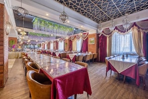 Un restaurant avec de longues tables, des plantes suspendues et un plafond orné de motifs.