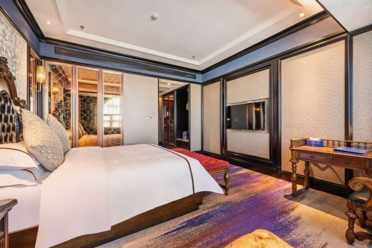 A spacious bedroom with a large bed, a wooden desk, and a view through a glass door.