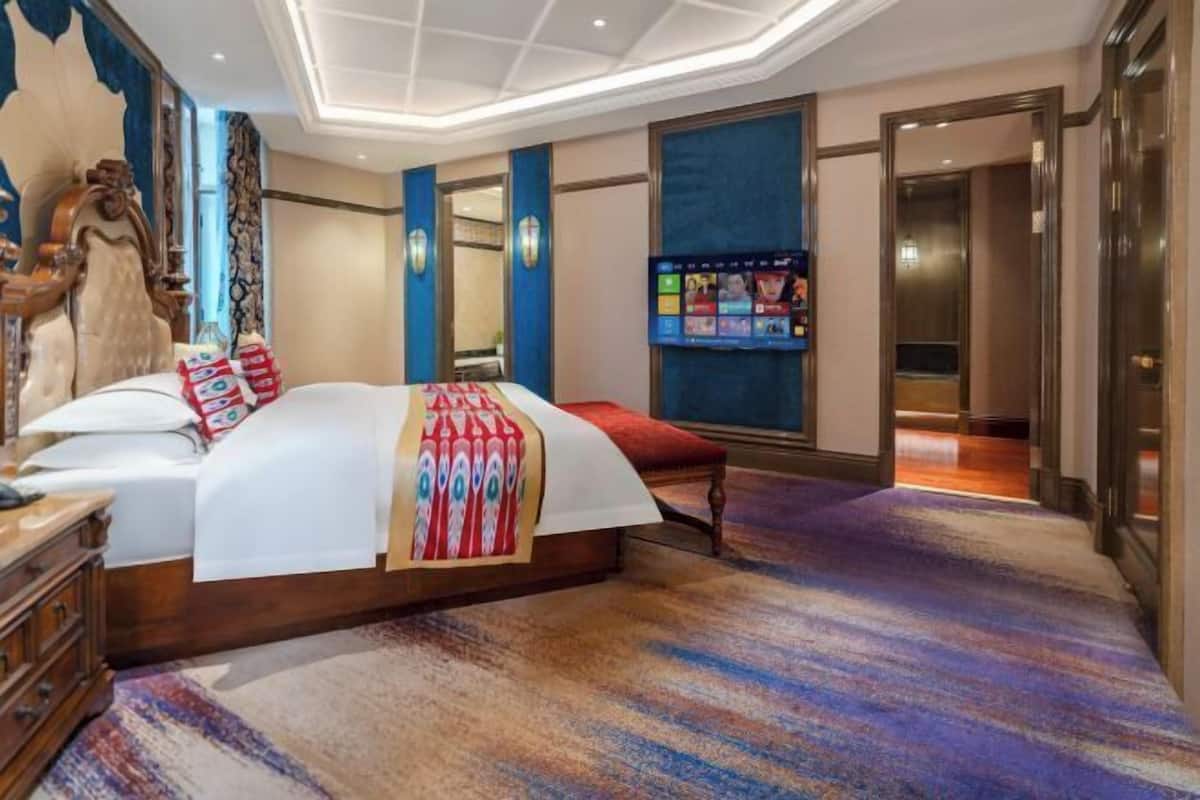 A spacious hotel room with a large bed, a wooden dresser, and a vibrant carpet.