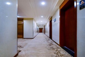 A hotel corridor with a carpeted floor, doors on both sides, and a sign indicating the direction to the elevator. - Qingzhu Hotel · Junxi Select (Chongqing)