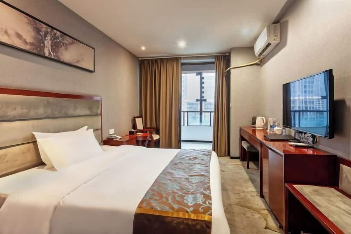 A hotel room with a large bed, a desk, a television, and a window with curtains.