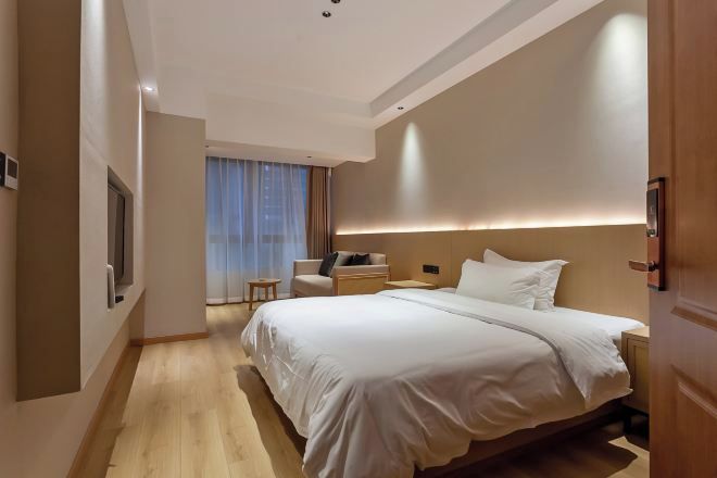 Una habitación de hotel moderna con una cama grande, un pequeño espacio de descanso y vistas a la ciudad desde la ventana.