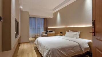 Una habitación de hotel moderna con una cama grande, un pequeño espacio de descanso y vistas a la ciudad desde la ventana.