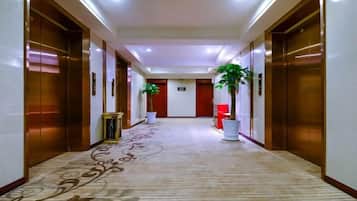 A hotel corridor with carpeted flooring, wooden doors, and potted plants.