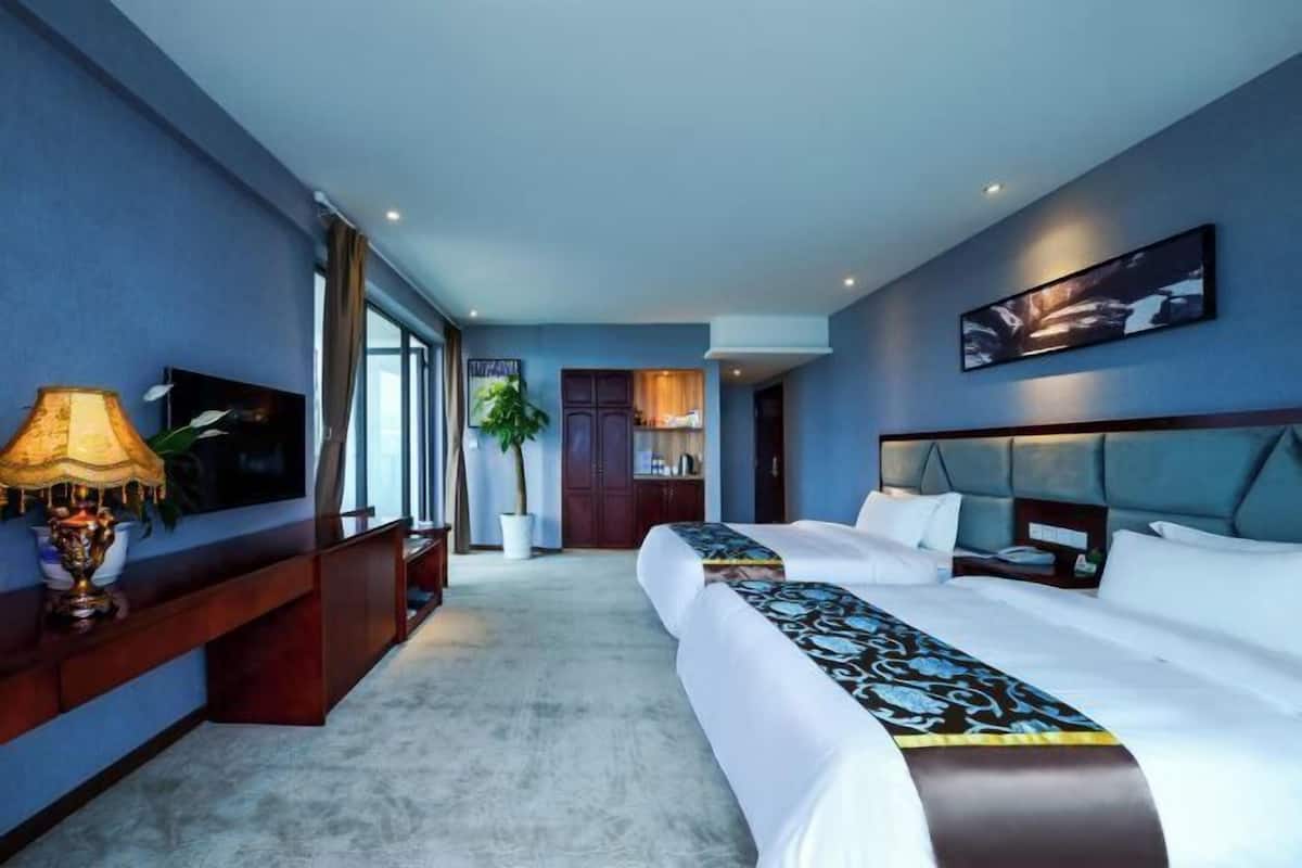 A hotel room with a large bed, a TV, a desk with a lamp, and a potted plant.