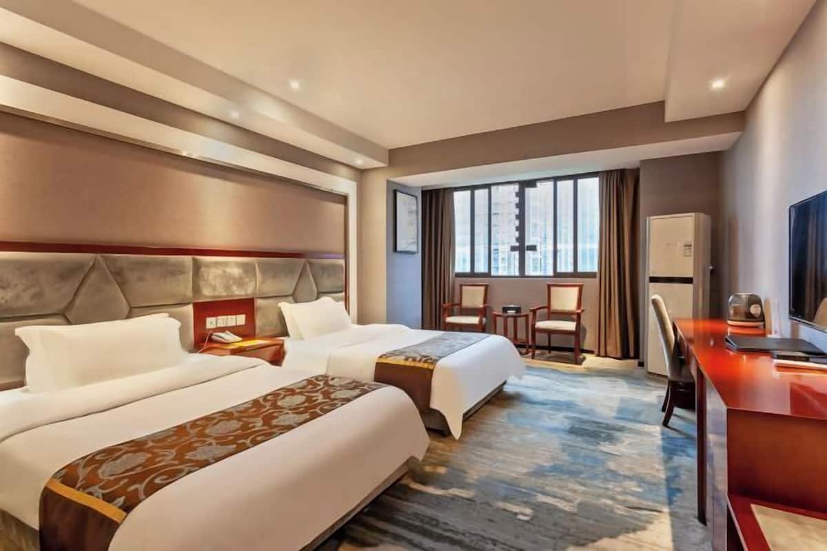 A hotel room with two beds, a desk, a chair, and a large window.