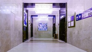 Ein mit Marmor ausgelegter Flur, ausgestattet mit einem Chandelier, gerahmten Kunstwerken und Informationspostern an den Wänden.
