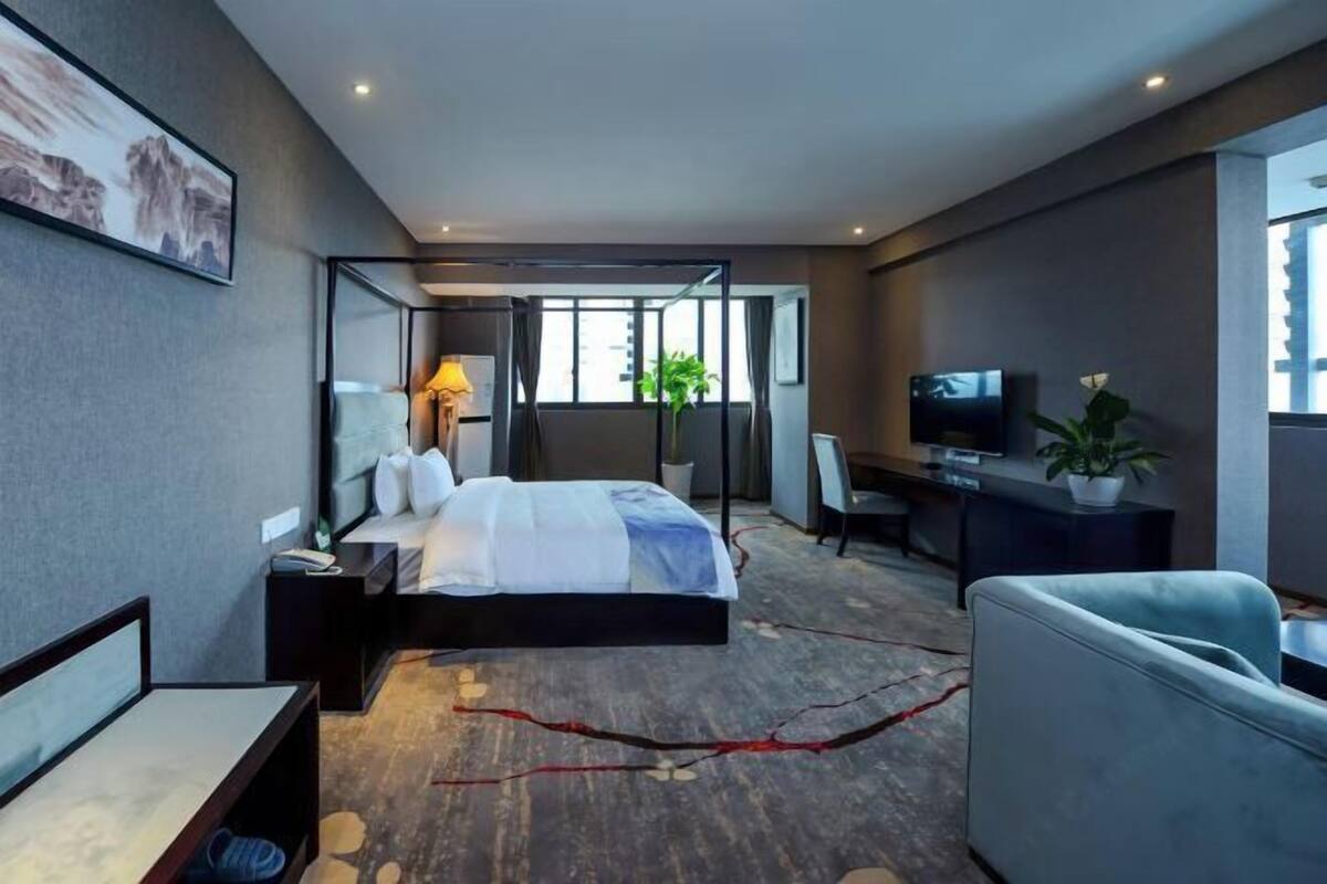 A modern hotel room with a bed, desk, TV, and seating area.