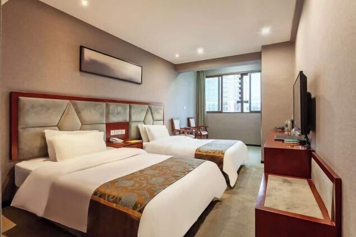 A hotel room with two beds, a desk, a chair, a television, and a window with a view.