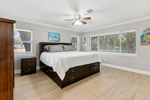 Un dormitorio con cama, ventilador de techo y ventanas amplias.