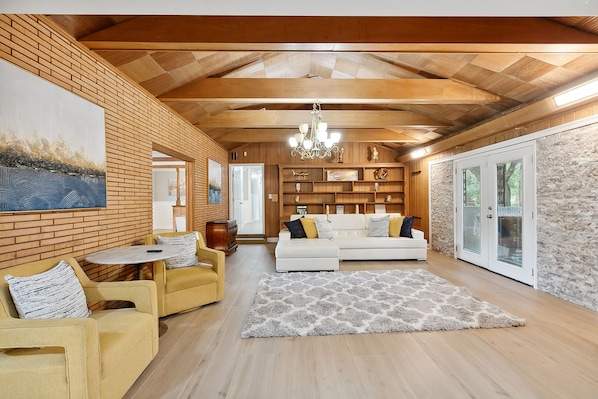 Amplia sala de estar con sofá blanco, sillones amarillos, techo de madera y un cuadro grande en la pared.