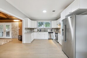 Una cocina moderna con armarios blancos, un refrigerador de acero inoxidable y un salpicadero de piedra.