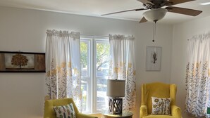 Una sala de estar con dos sillones amarillos, un ventilador de techo, una mesa de centro y un tapete estampado.