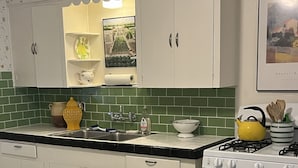 Una cocina con armarios blancos, salpicadero verde y una mesa de comedor con platos y tazas amarillas.