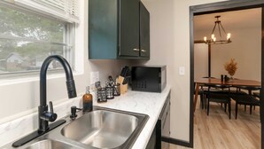 A modern kitchen with a stainless steel sink, black cabinets, a microwave, and a dining area with a chandelier. - Amazing East Side 3BR 2BA Wifi SMRT TV (Wichita)