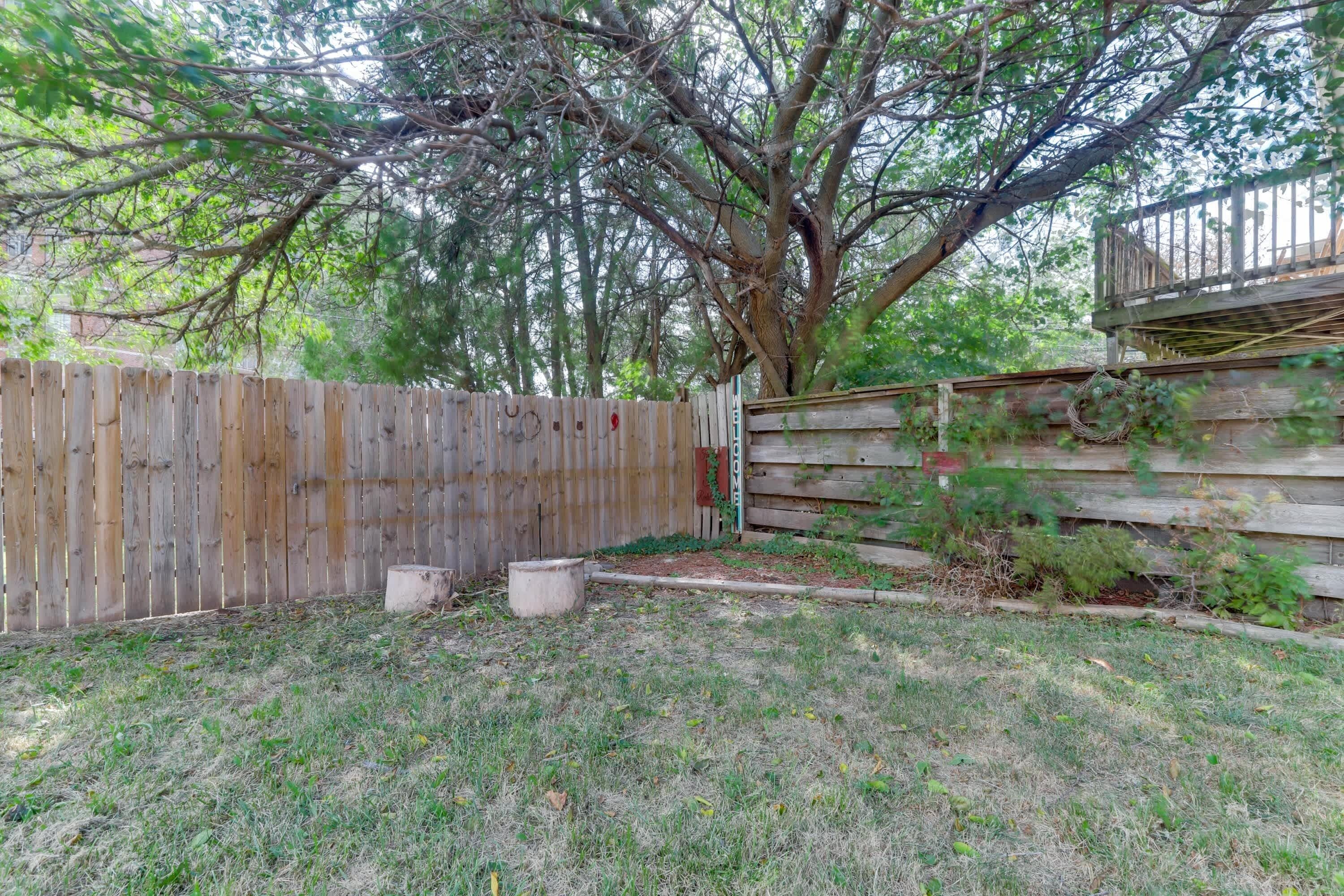 A backyard with a wooden fence, a tree, and a wooden deck.