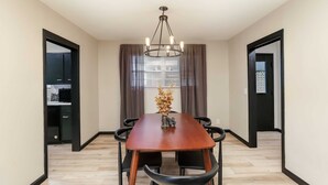A dining area with a wooden table, black chairs, a chandelier, and a view through a window with curtains. - Amazing East Side 3BR 2BA Wifi SMRT TV (Wichita)