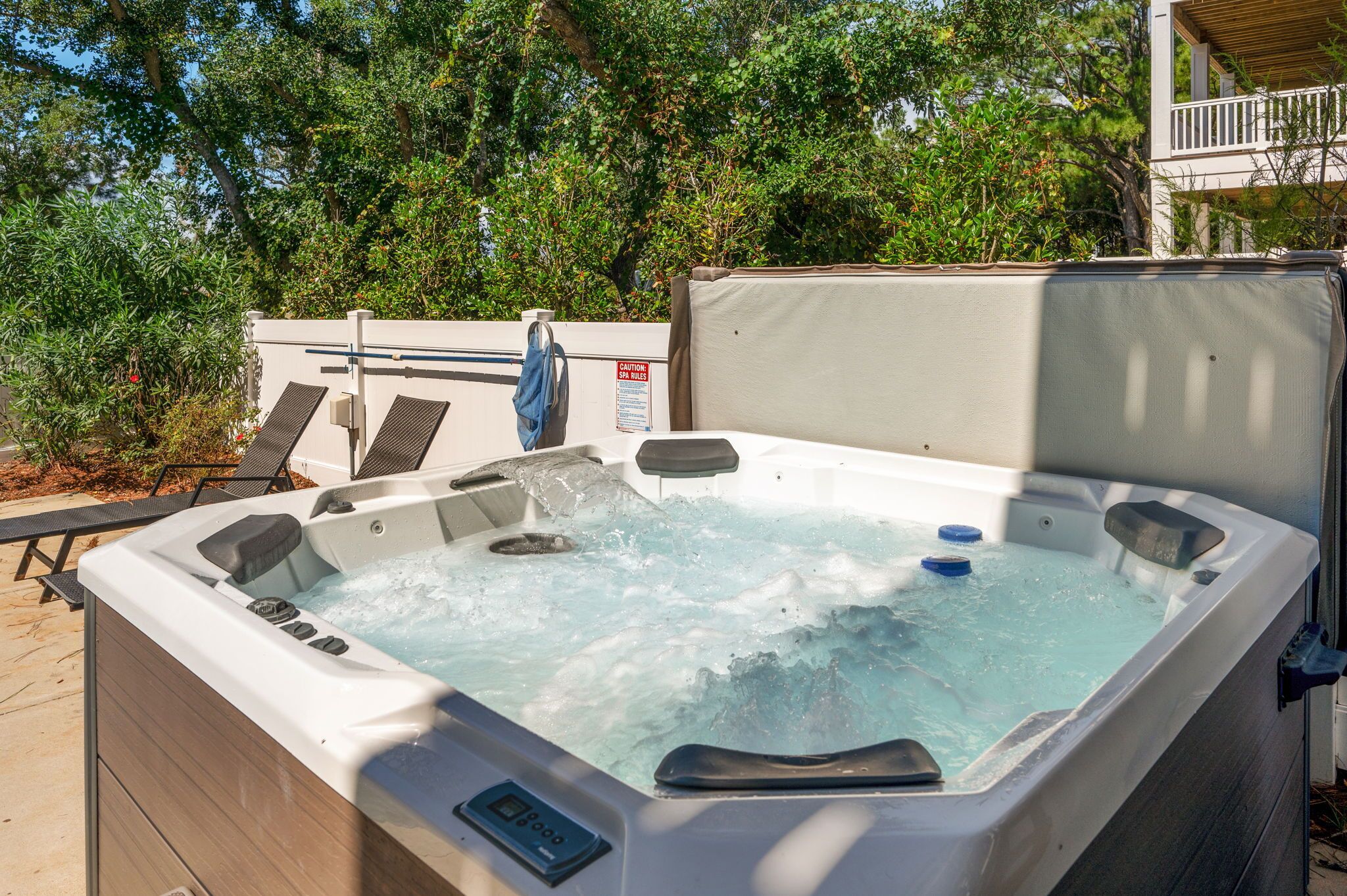Un jacuzzi con panel de control, rodeado de mobiliario exterior y abundante vegetación.