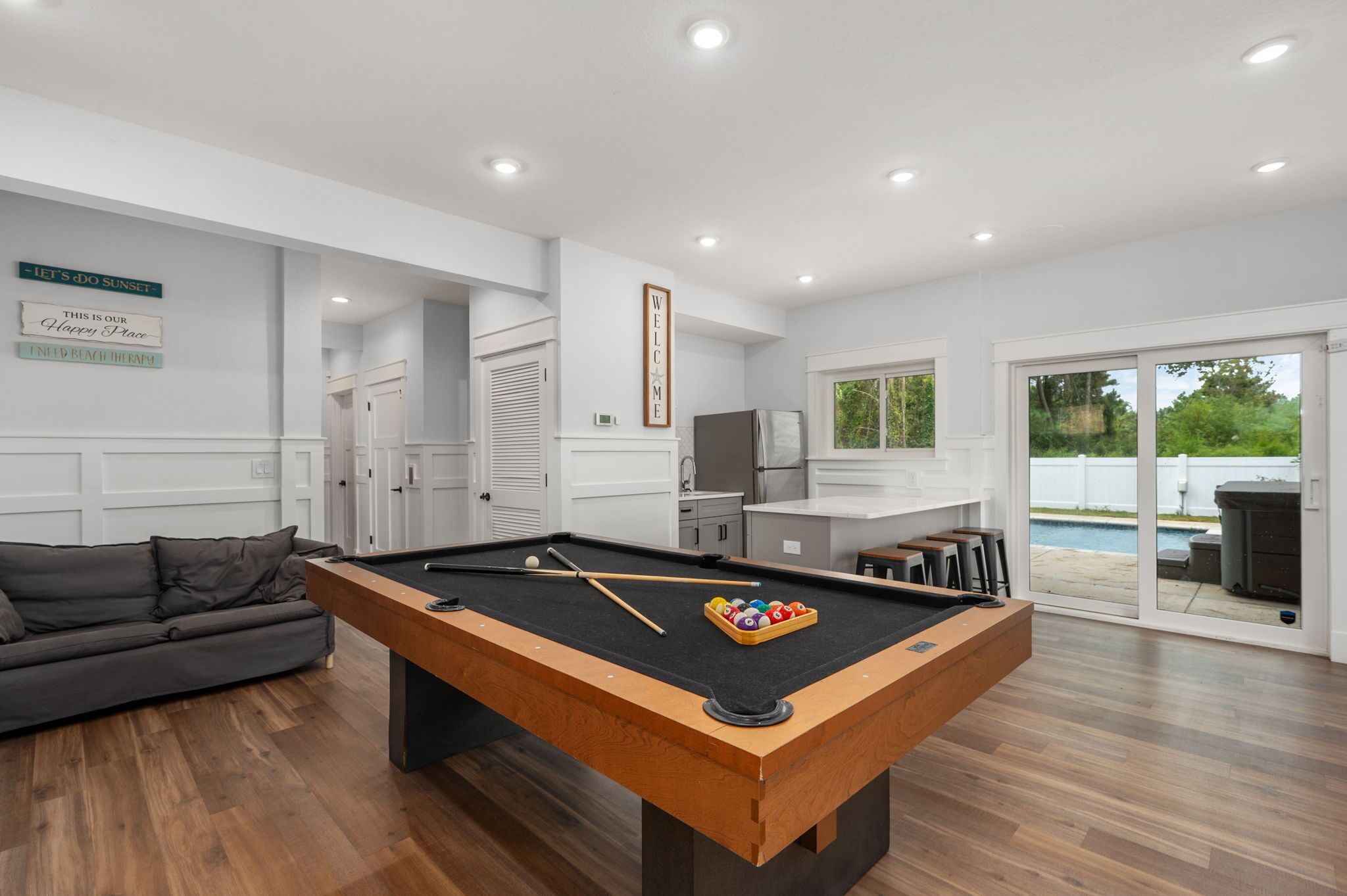 En moderne stue med et billardbord, en sofa og udsigt til en have med swimmingpool.