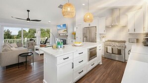 A spacious kitchen with white cabinetry, a large island, and stainless steel appliances. There is a ceiling fan and pendant lights above the island. - Last-Minute! Soundfront, Pool, Hot Tub, Elevator, Renowned Currituck Club Access (Corolla)