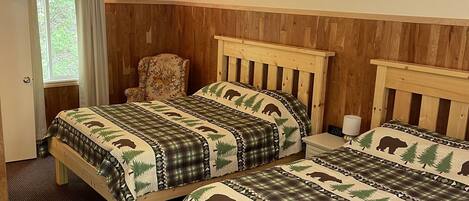 A room with two wooden beds, a chair, a nightstand, and a window with curtains.