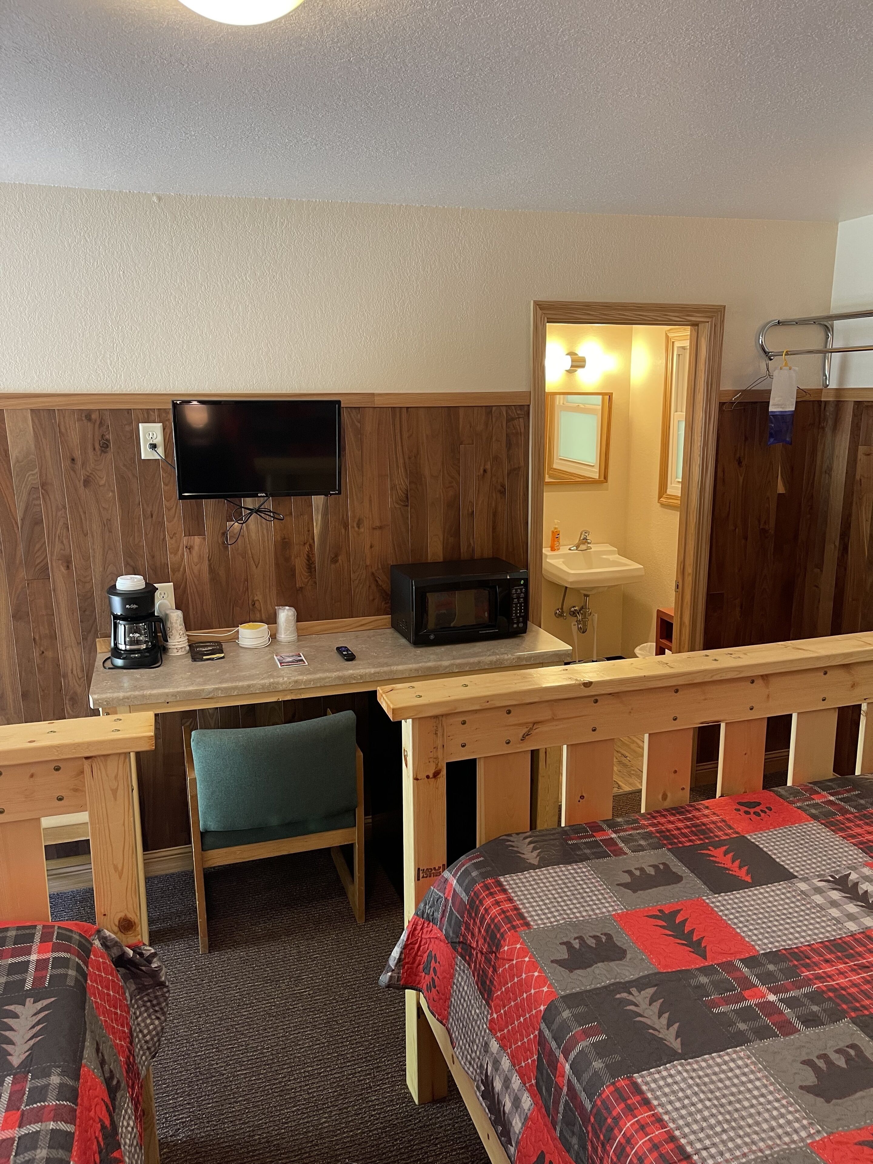 Une chambre d’hôtel avec un bureau en bois, un four à micro-ondes, une machine à café, une télévision, un lavabo et un lit recouvert d’une couverture à motifs.