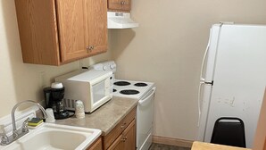 Una cocina compacta con armarios de madera, una estufa blanca, un microondas, un lavamanos y una pequeña mesa.