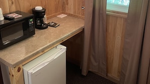 Una kitchenette compacta con microondas, cafetera y refrigerador pequeño.