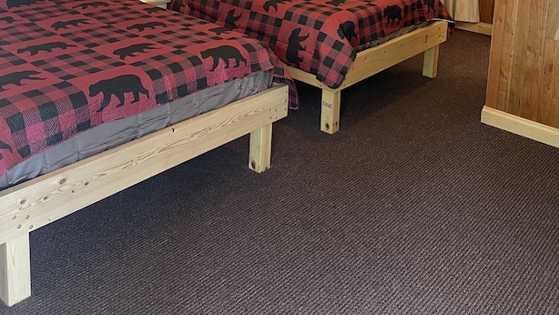 Una habitación con dos camas de madera, suelo alfombrado y paneles de madera en las paredes.