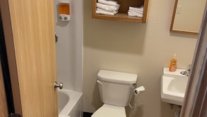 Un baño con inodoro, lavamanos, estante de madera con toallas, ducha y espejo.